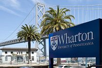 A sign for Wharton University of Pennsylvania in front of palm trees and a bridge, likely representing the school''s presence in a city.