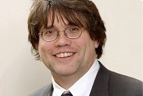 Headshot of a person wearing glasses and a suit, smiling at the camera.