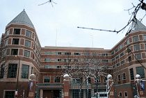 A large, brick building with turrets at the corners, featuring multiple windows and a central entrance, under a cloudy sky.