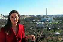 A person in a red outfit standing outdoors with a view of the White House and the Washington Monument in the background.